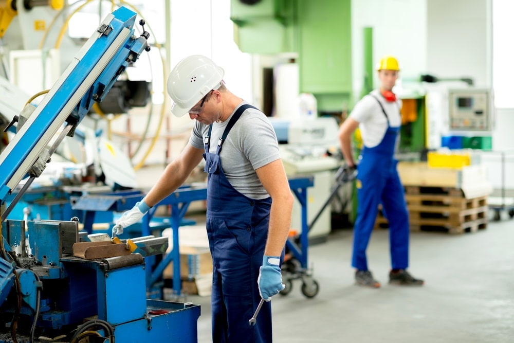 worker in protective clothing in factory using machine