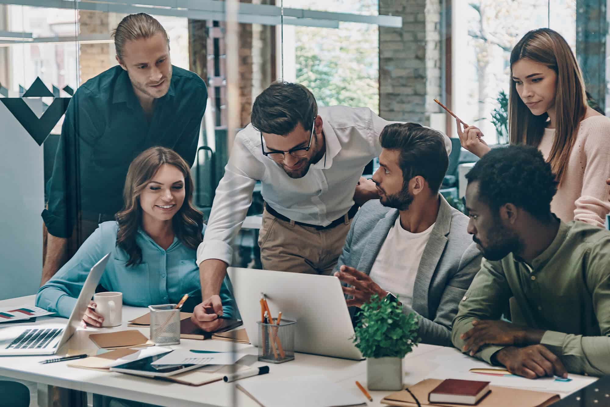 Group of young modern people in smart casual wear communicating and using modern technologies while working in the office