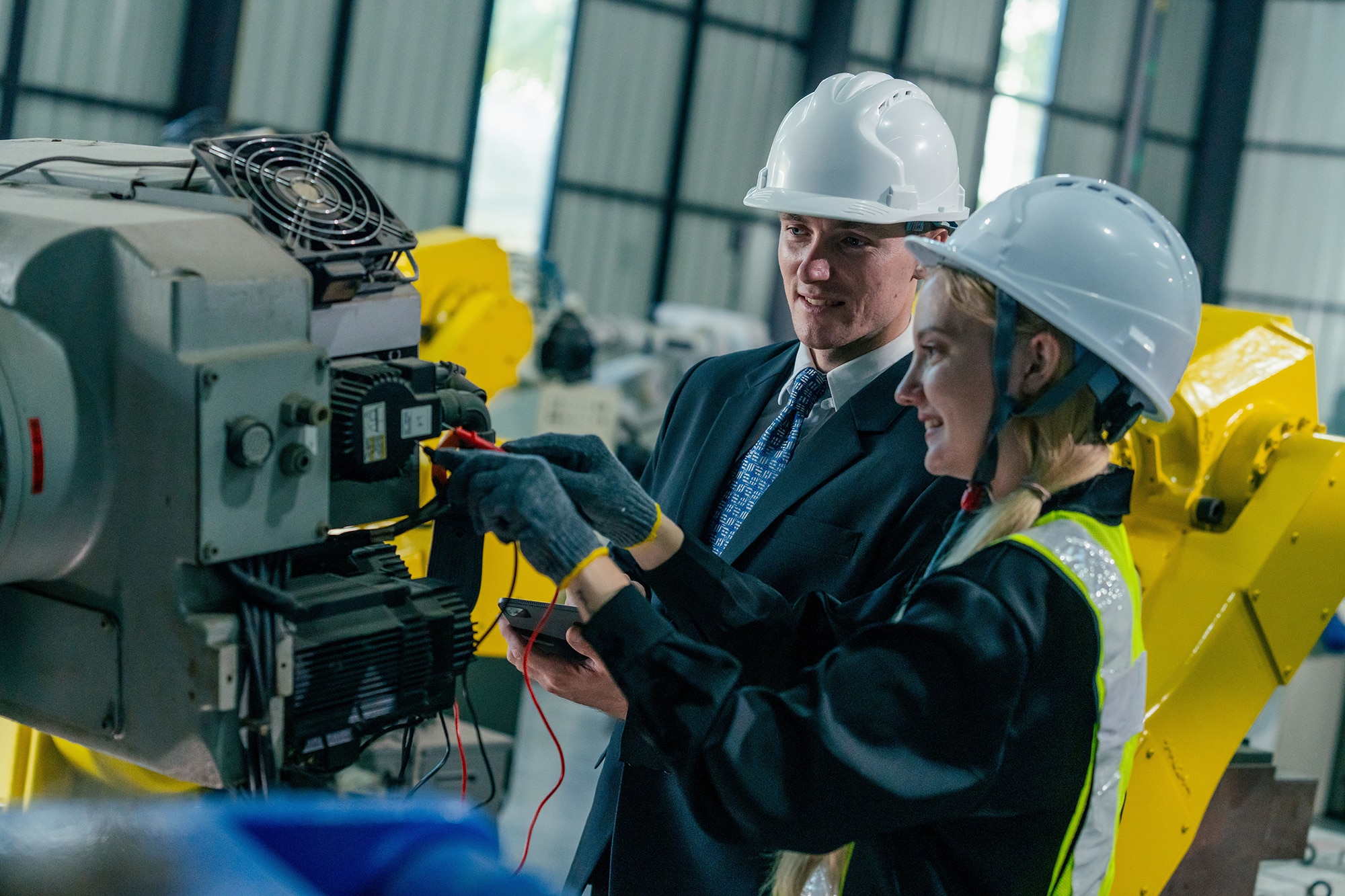A business professional and a female technician examine equipment inside an industrial plant.