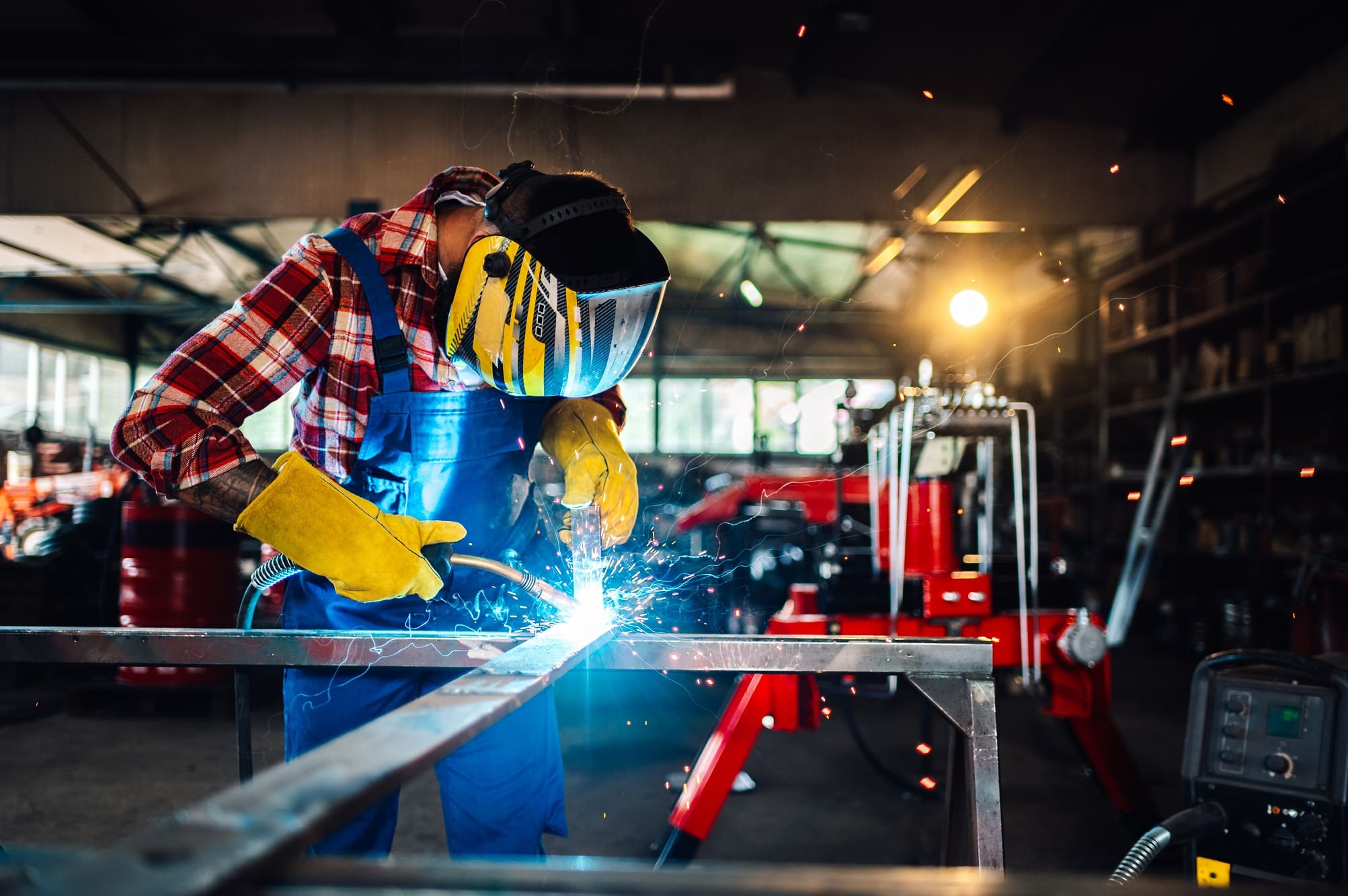 Dark haired man working hard in a workshop while welding a metal construction