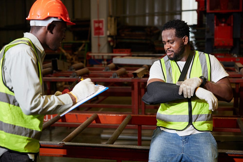 Injured Factory Worker Undergoing Arm Injury Evaluation in Safety Vest with Supervisor