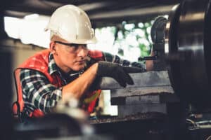 Focused manufacturing worker in safety gear operating machinery in industrial facility, demonstrating skills for temp-to-perm career growth.