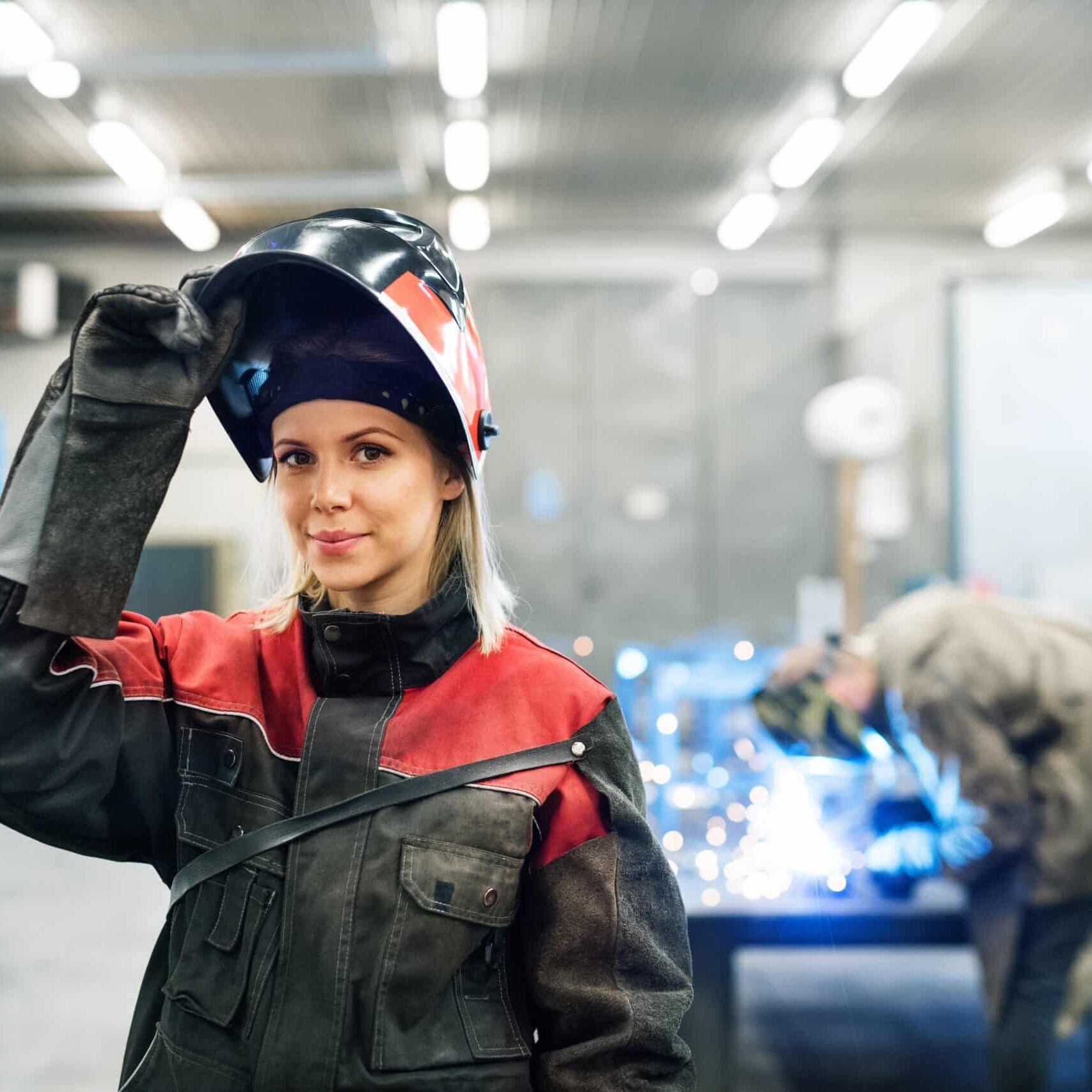 Beautiful blonde woman works as a welder in workshop, operating welding machine