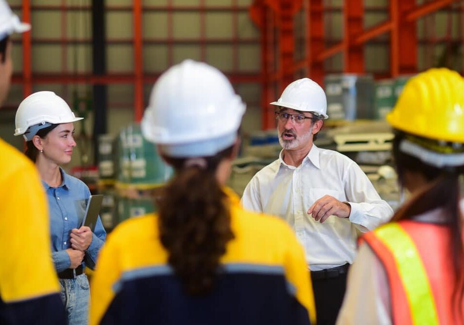 Industrial Team Safety Meeting in Warehouse with Hard Hats and High-Visibility Gear